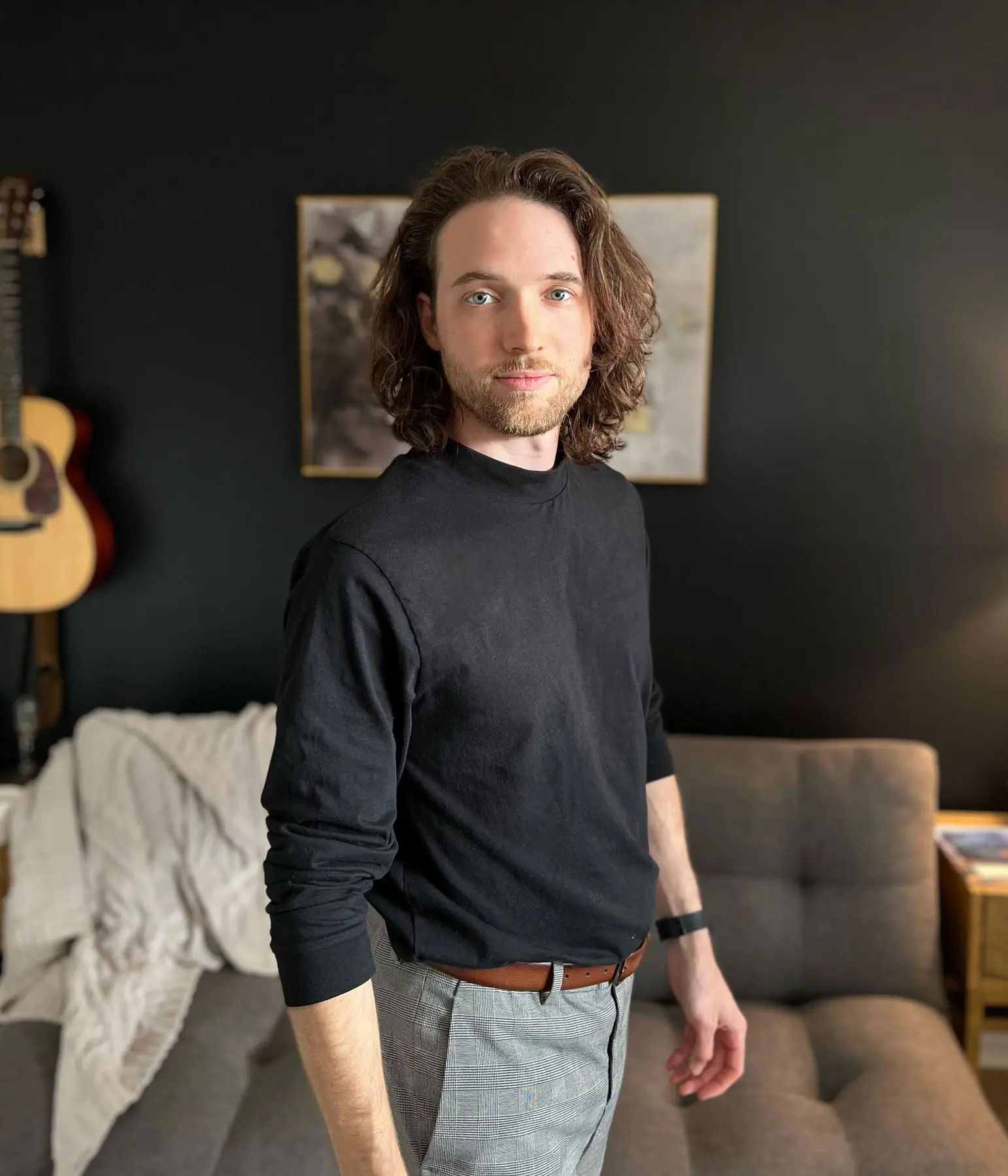 Jonathan Puckett standing in a living room with a guitar and framed art behind him.